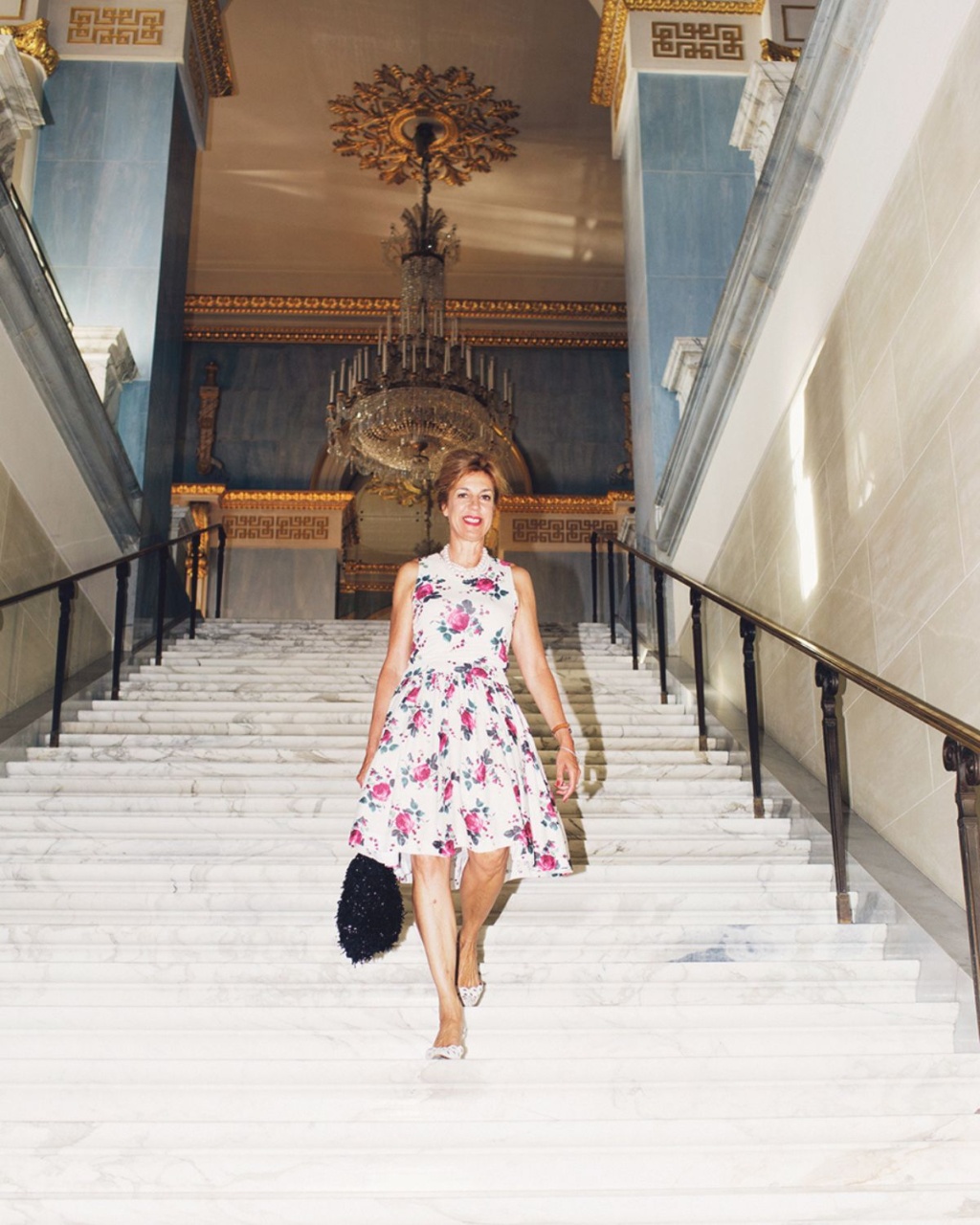 A woman in a floral dress poses in a display window, surrounded by mannequin heads and various decorative items.
