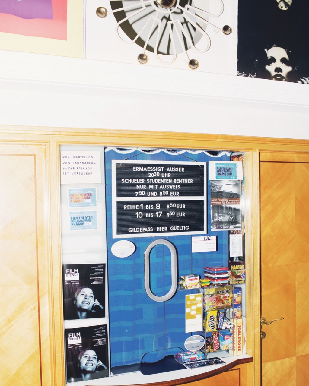 A ticket booth with pricing information for students and seniors, surrounded by colorful promotional materials and a vintage fan above.