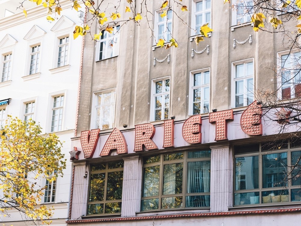 Historic theater facade with "Variete" in large, retro-style letters. Autumn leaves partially frame the beige building, conveying a nostalgic feel.