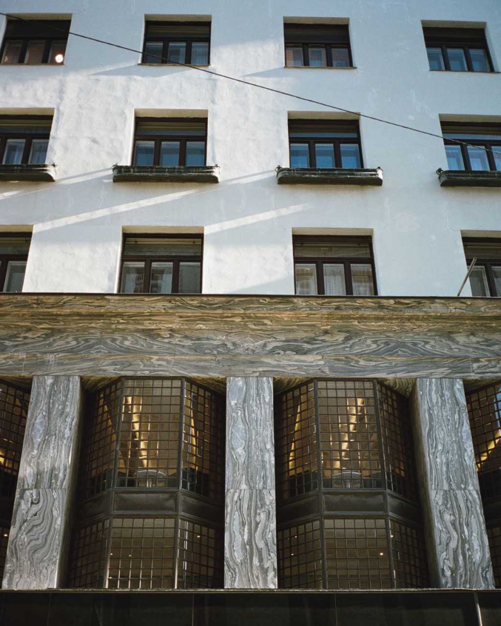 Facade of a modernist building with large geometric windows and distinctive marble columns. The clean lines and symmetry create a sleek, contemporary feel.