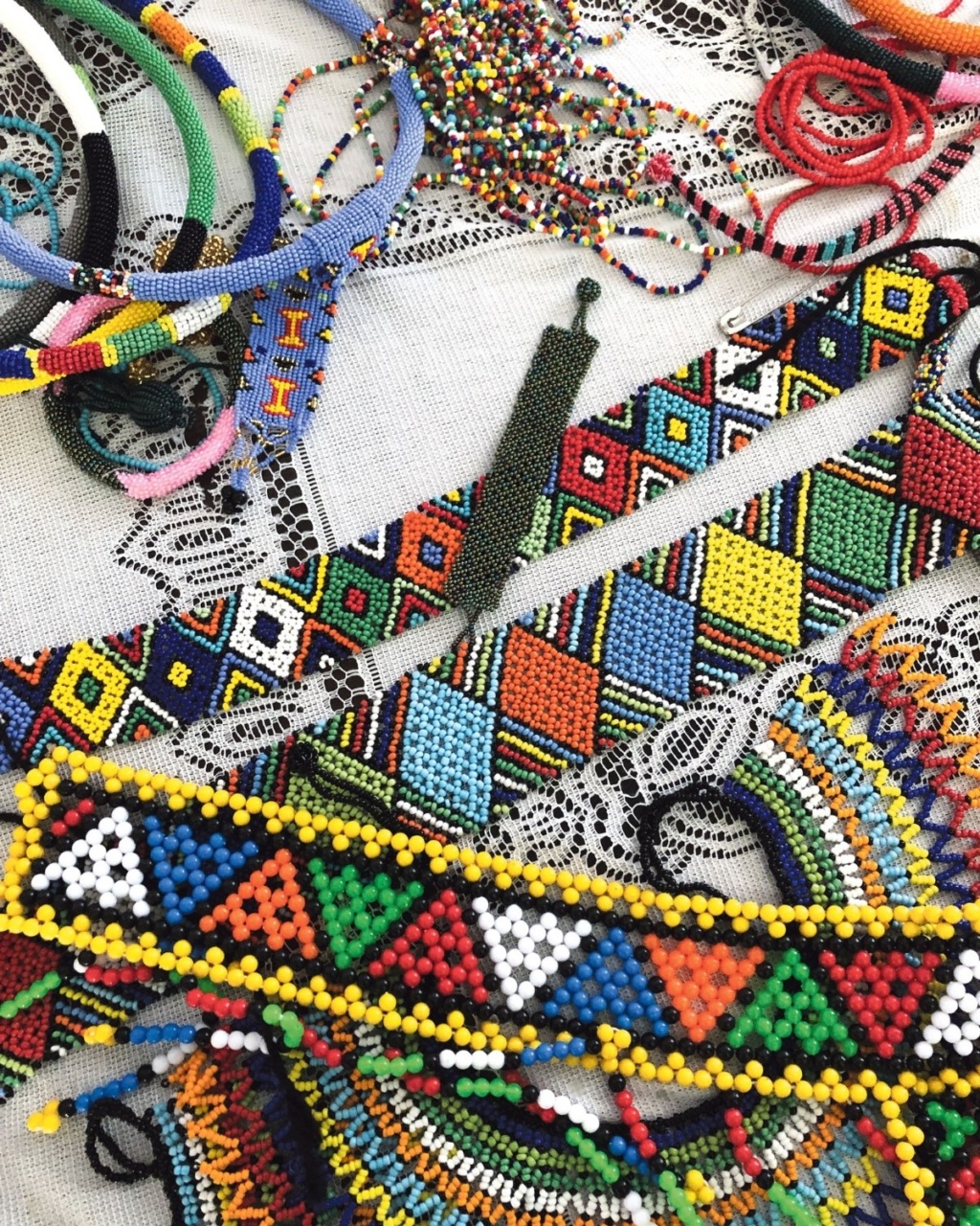 A vibrant assortment of beaded jewelry, including colorful bracelets and necklaces with geometric patterns, lies on a delicate lace fabric.