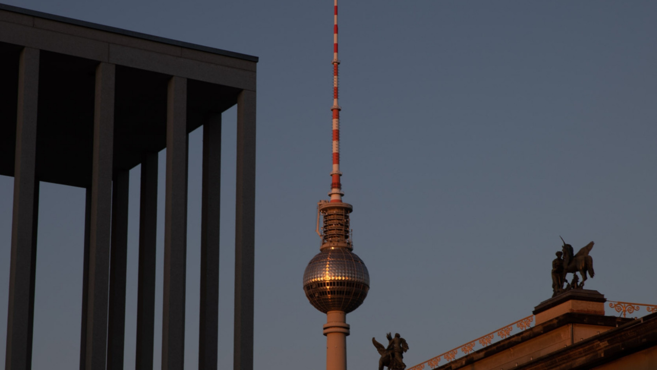 The image shows Berlin's TV Tower at sunset with a clear sky. Modern and classical architecture frame the scene, evoking a blend of history and progress.