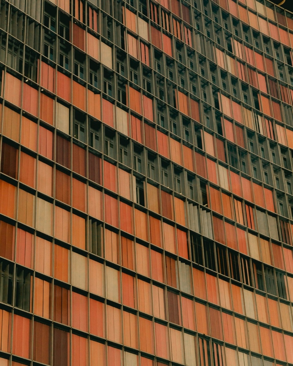 Curved building facade with a grid of warm-toned rectangular windows in shades of red and orange. Creates a retro and geometric pattern.