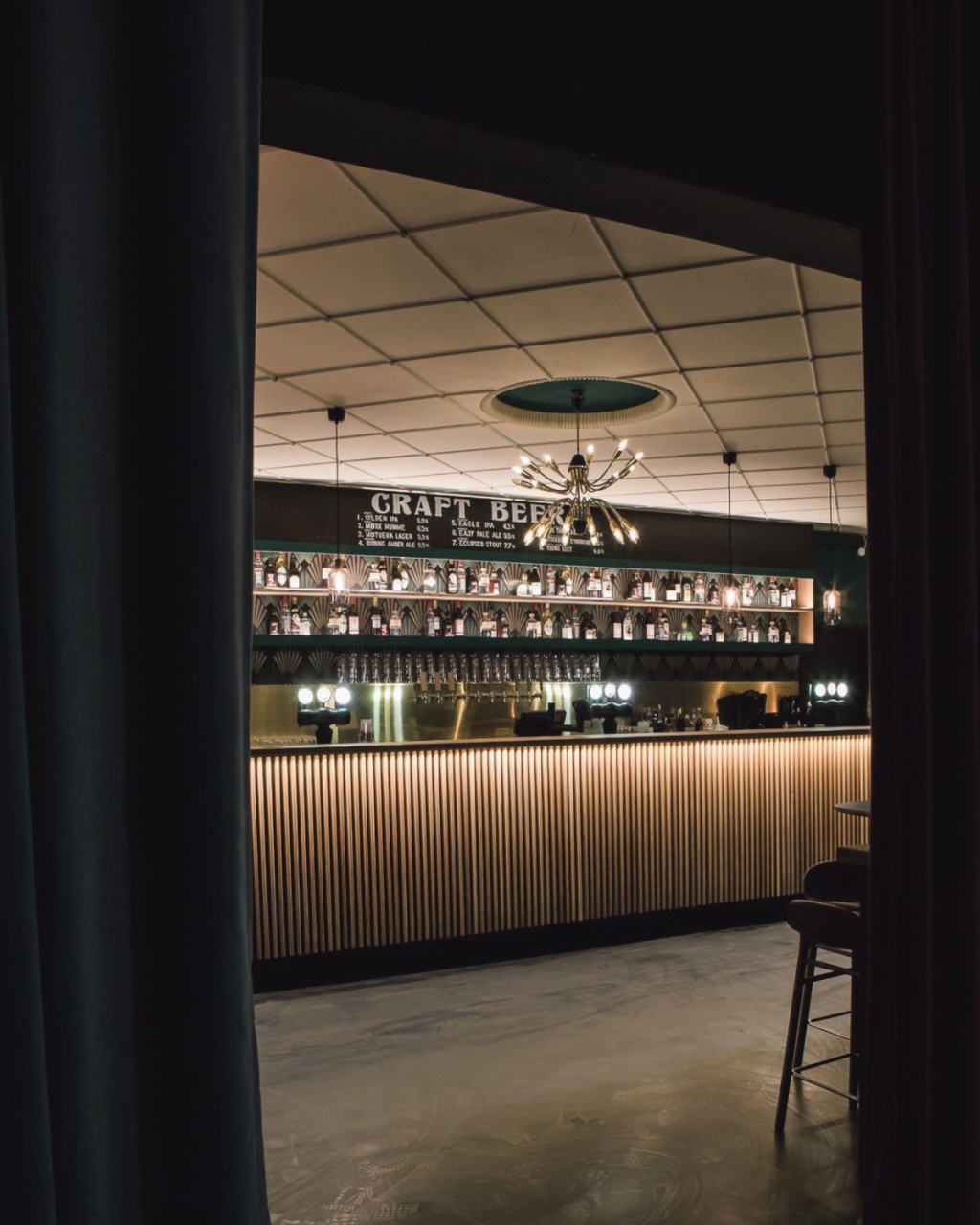 Chic bar interior with a modern design, featuring a backlit wooden counter and shelves displaying various bottles. The atmosphere feels sophisticated and inviting.