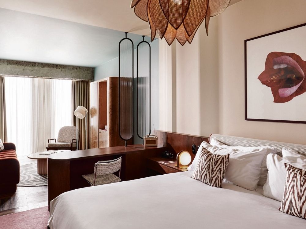 Stylish hotel room with a modern vibe, featuring a large bed, zebra-patterned pillows, abstract art, and a sculptural light fixture.