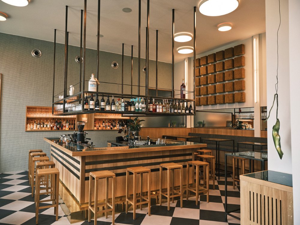 Stylish bar interior featuring a wooden counter, shelves with various bottles, and modern seating in a chic, contemporary design.