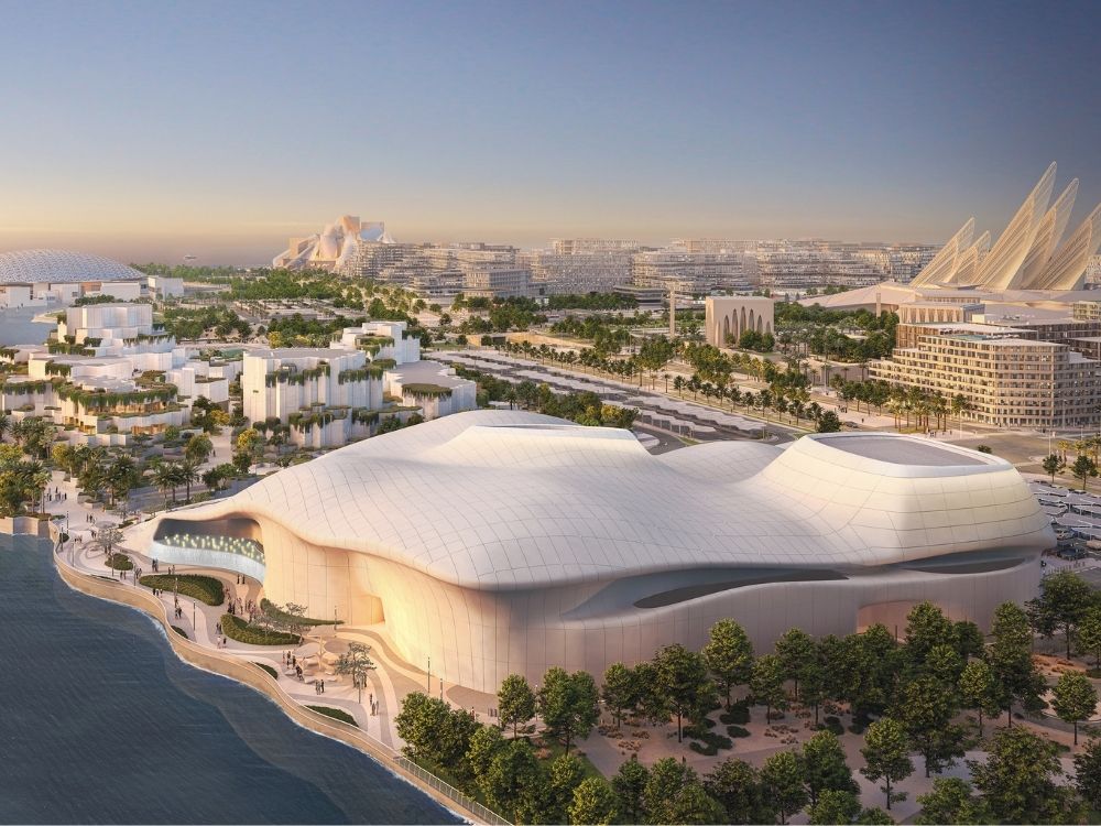 Futuristic waterfront cityscape at sunset, featuring modern, flowing architecture with white domes and lush greenery lining the coast.