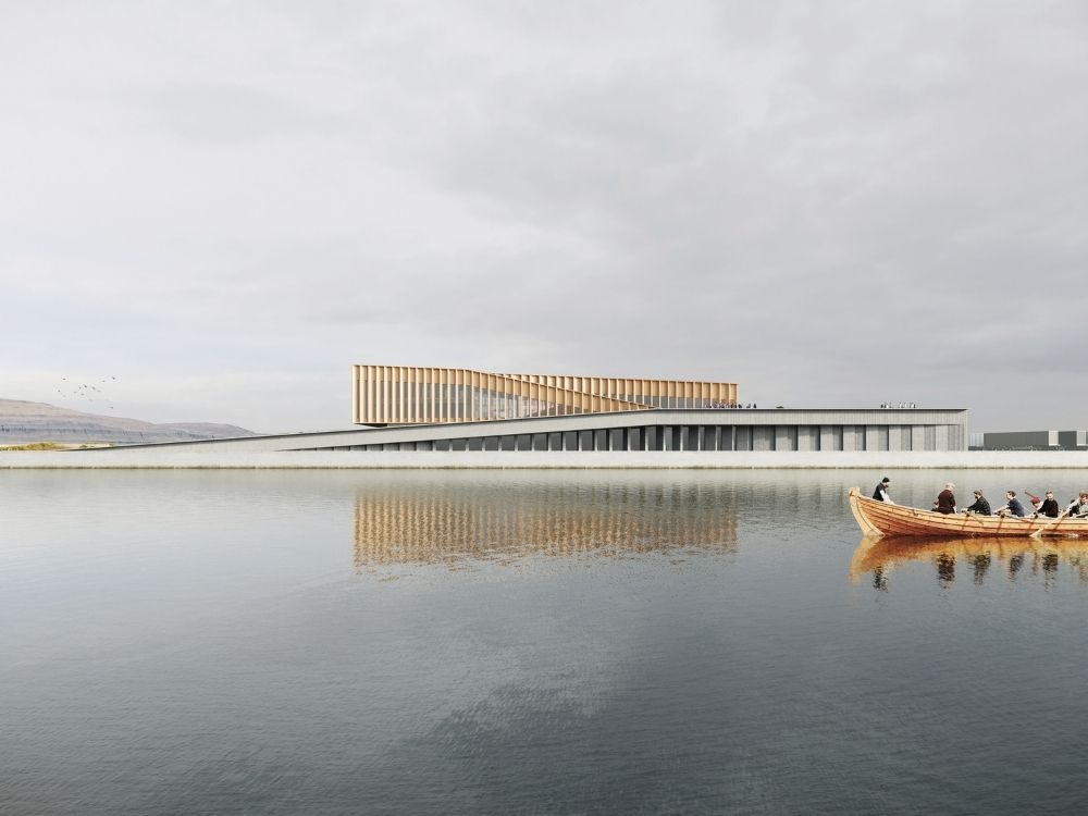 A modern, low-profile building with vertical slats is reflected in a calm lake under a cloudy sky. A small, wooden boat with people is rowing by.