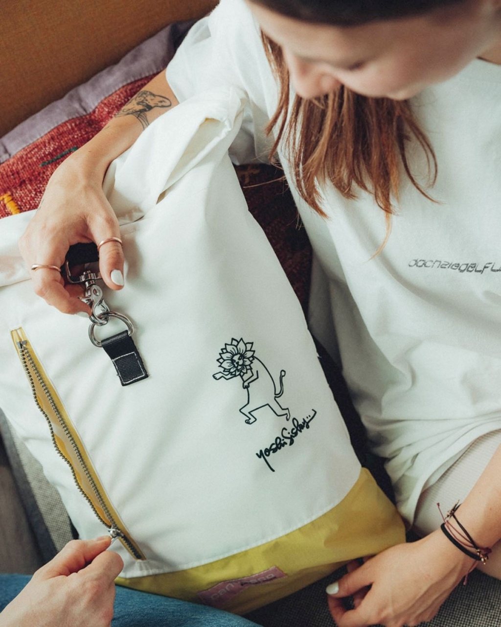 Woman holding white and yellow backpack with playful lion drawing and black clip.