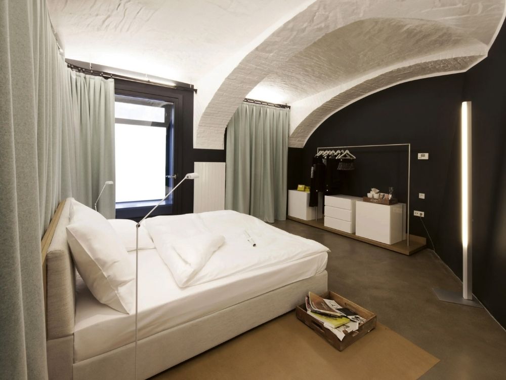 Modern bedroom with arched ceiling and soft lighting. Features a large bed, minimalist decor, open closet with hanging clothes, and floor lamp.