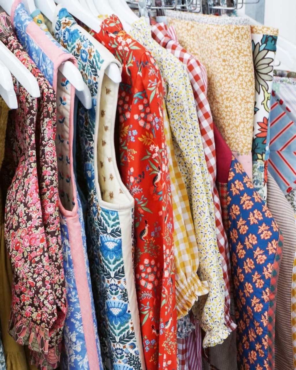 A rack of colorful dresses with various floral and patterned designs hang closely together.