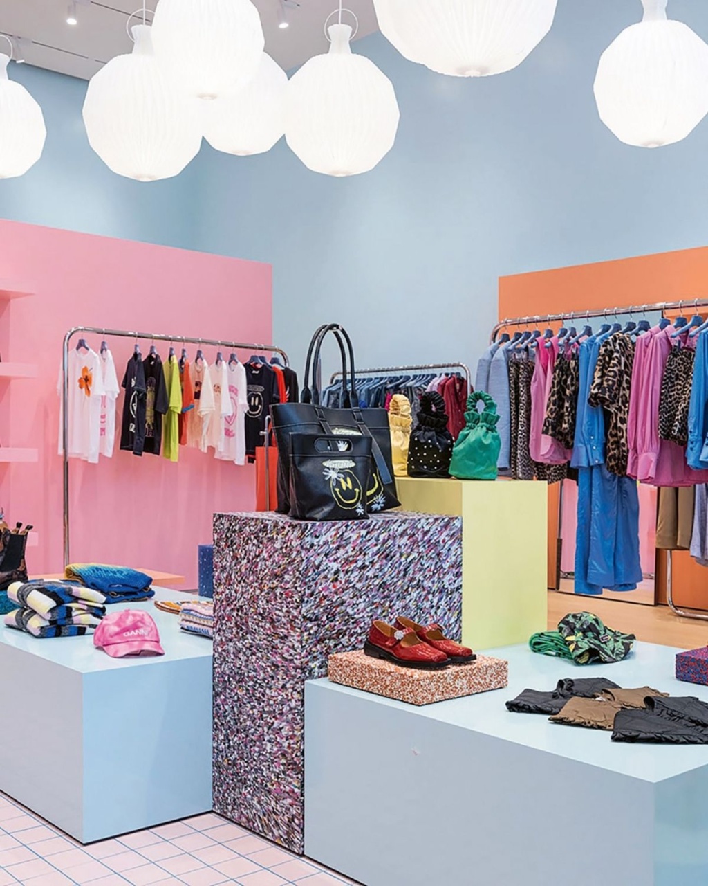 Bright, colorful boutique with pastel pink and blue walls, racks of vibrant clothing, white pendant lights, and displays of accessories and bags.