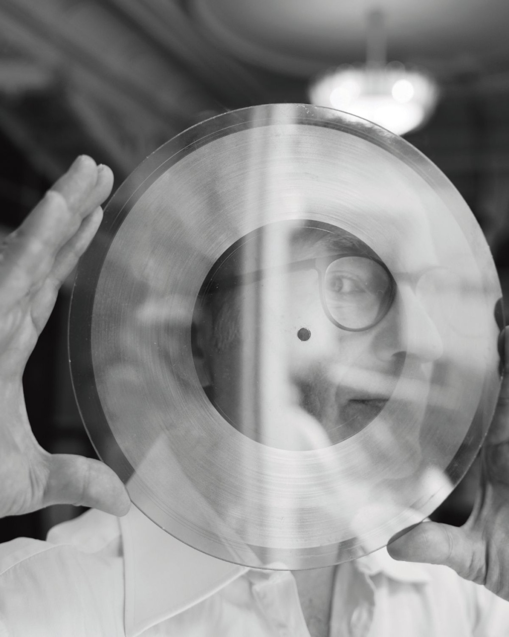 Black-and-white photo of a person holding a clear record up to their face, creating a layered, reflective look.