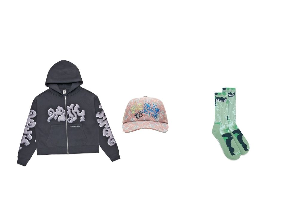 Dark gray hoodie with gray abstract patterns, pink cap with blue graffiti and floral design, and mint green socks with navy accents on a white background.