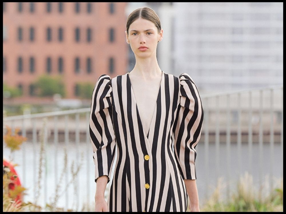 A model sports a black and white striped dress with puffed shoulders, against an urban background.