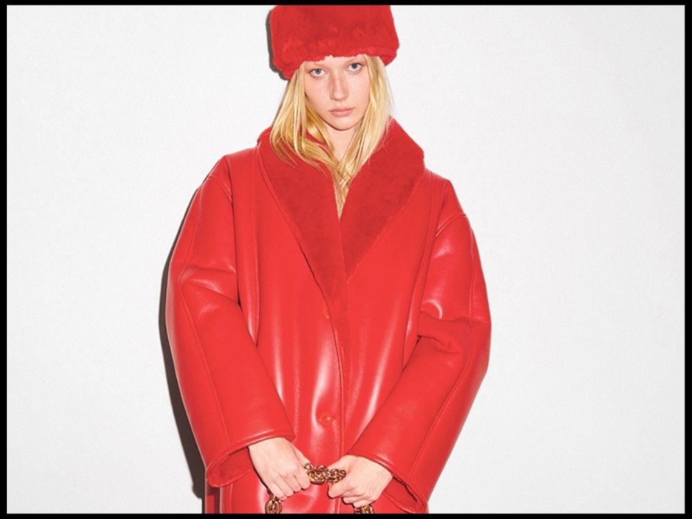 A person stands against a white background wearing an oversized red coat and matching furry hat.