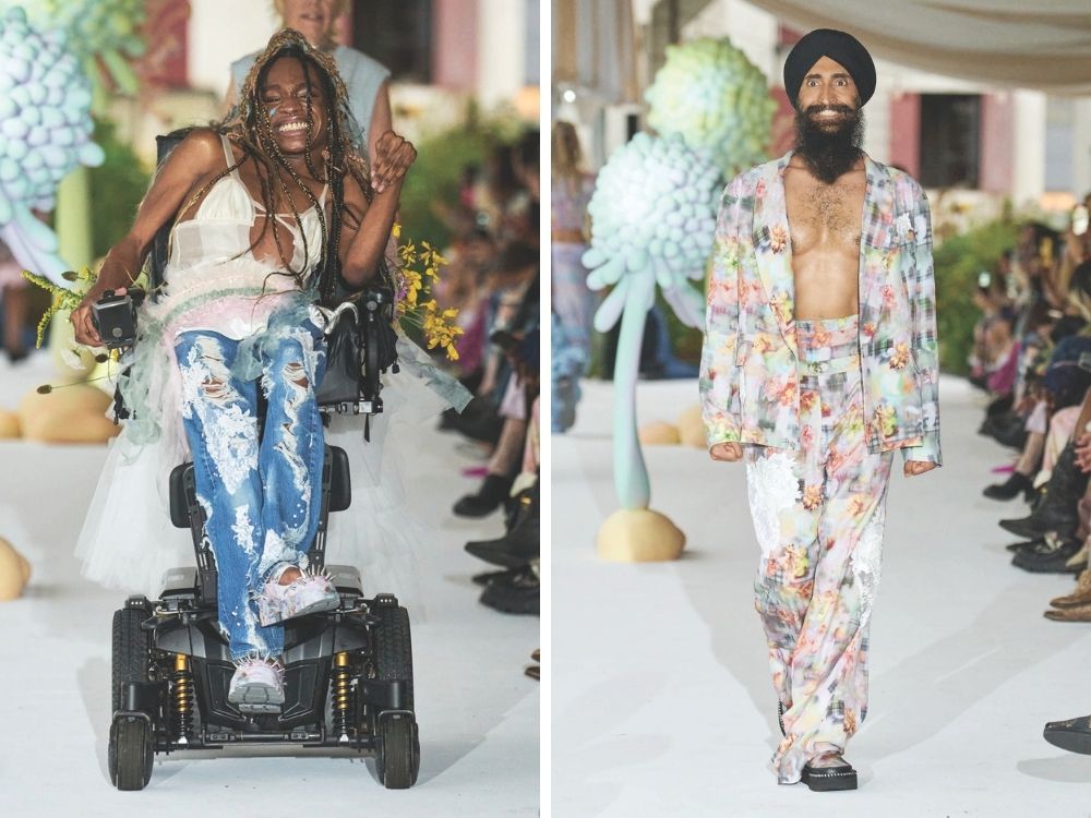 Two models on a runway. Left: A smiling model in a wheelchair, wearing distressed jeans and a tulle top, holds yellow flowers. Right: A model in a colorful floral suit, open shirt, and turban, walks confidently.