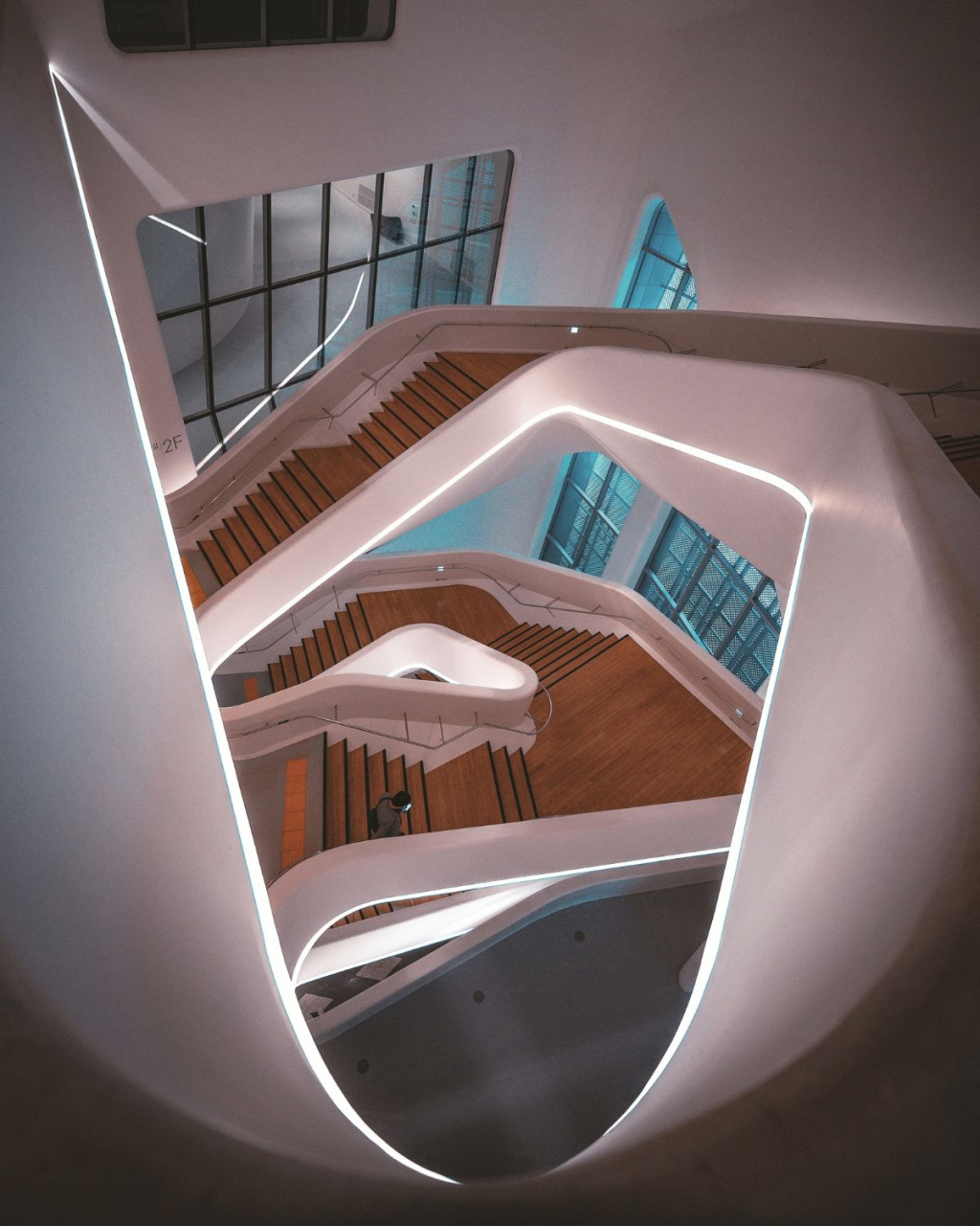 Looking down through a sculptural white spiral staircase with warm wooden steps and glowing edge lights.