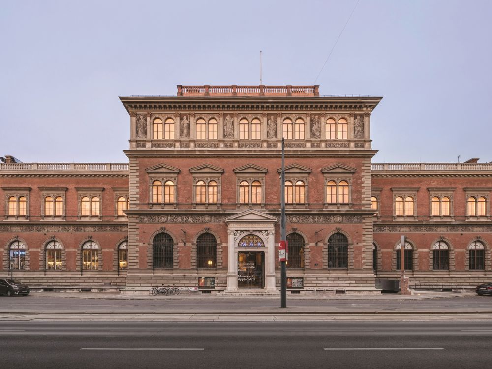 Symmetrical red-brick historic building with ornate stone trim and rows of glowing windows at dusk.