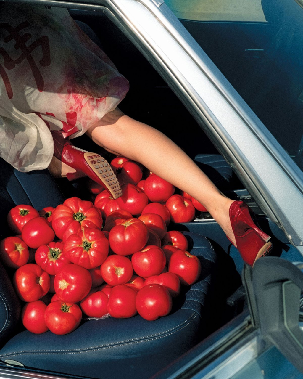 A person reaches into a car, holding a remote above a seat piled with ripe red tomatoes